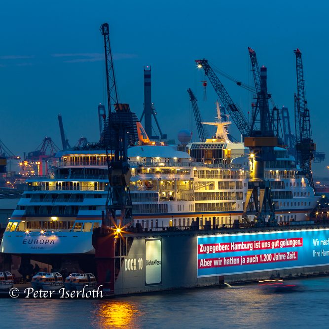 Ein beleuchtetes Schiff im Hafen, umgeben von Kränen bei Dämmerungslicht.