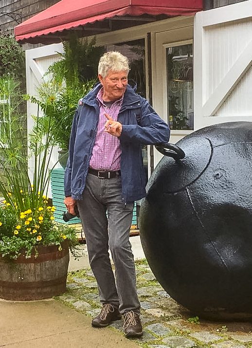 Ein Mann mit grauen Haaren steht neben einer großen schwarzen Kugel, während er nachdenklich schaut.