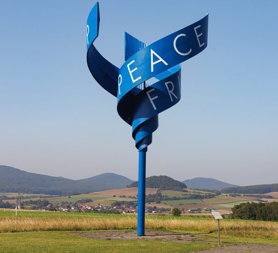 Blauer, spiralförmiger Skulptur mit dem Wort "Frieden" in großen Buchstaben.