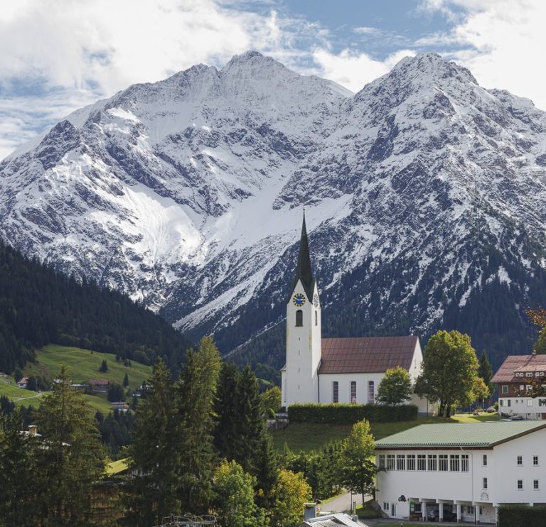 Berglandschaft mit schneebedeckten Gipfeln und einer Kirche im Vordergrund.