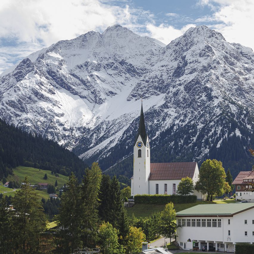 Alpenlandschaft mit schneebedeckten Bergen und einer Kirche im Vordergrund.