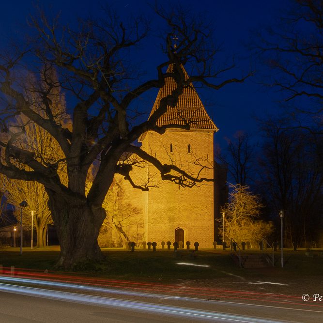 Mittelalterlicher Turm bei Nacht, umgeben von Bäumen und sanfter Beleuchtung.