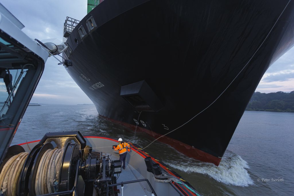 Großes Containerschiff fährt in ruhigem Wasser, mit einem kleinen Boot in der Nähe.